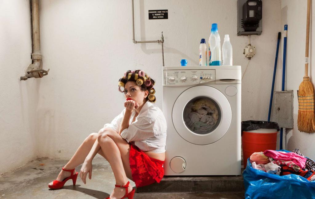Жена в купальнике забрасывает одежду в стиралку фото